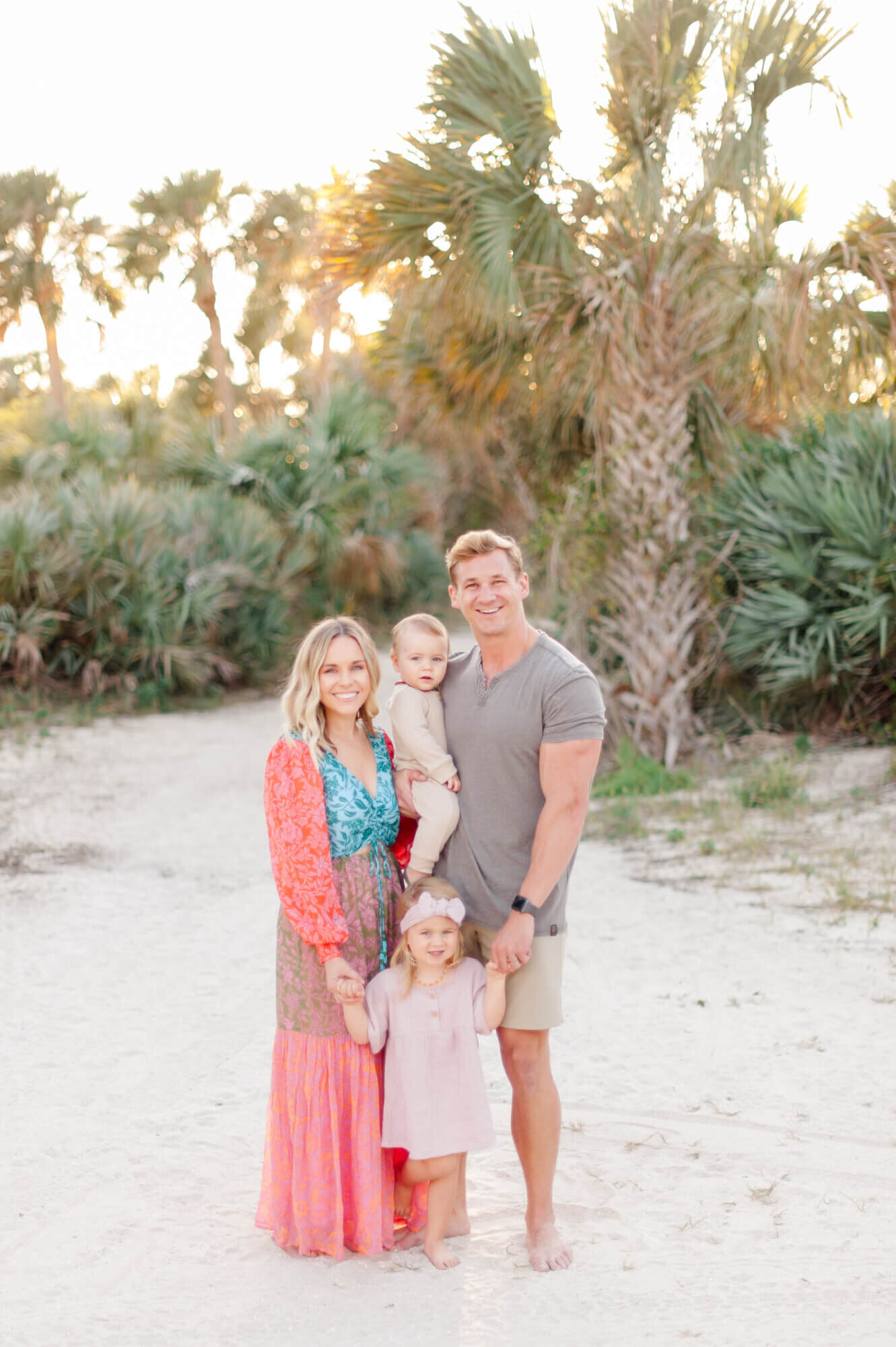 Family of four standing with beautiful Florida greenery behind them and a gorgeous sunset