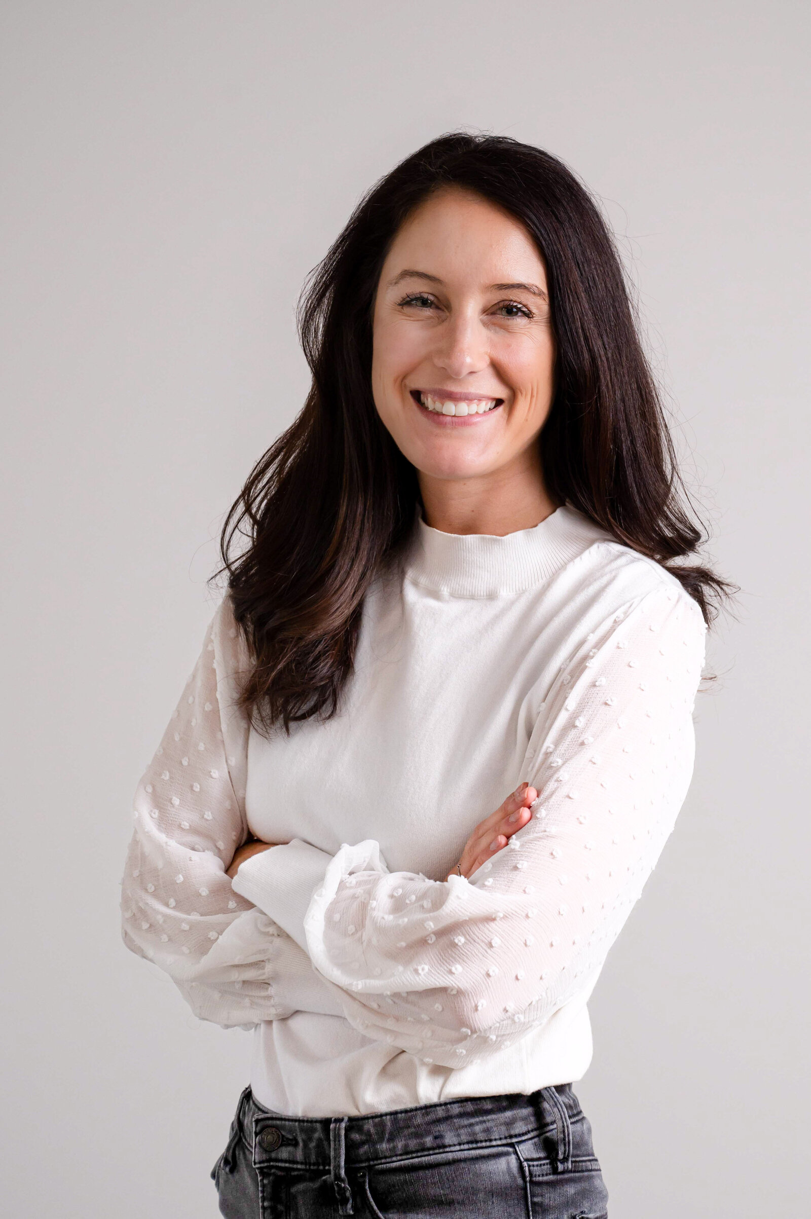 Headshot of a brunette woman in a white top with arms crossed.