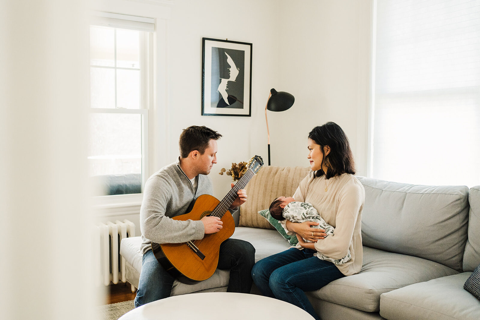 dad plays guitar to newborn baby in living room