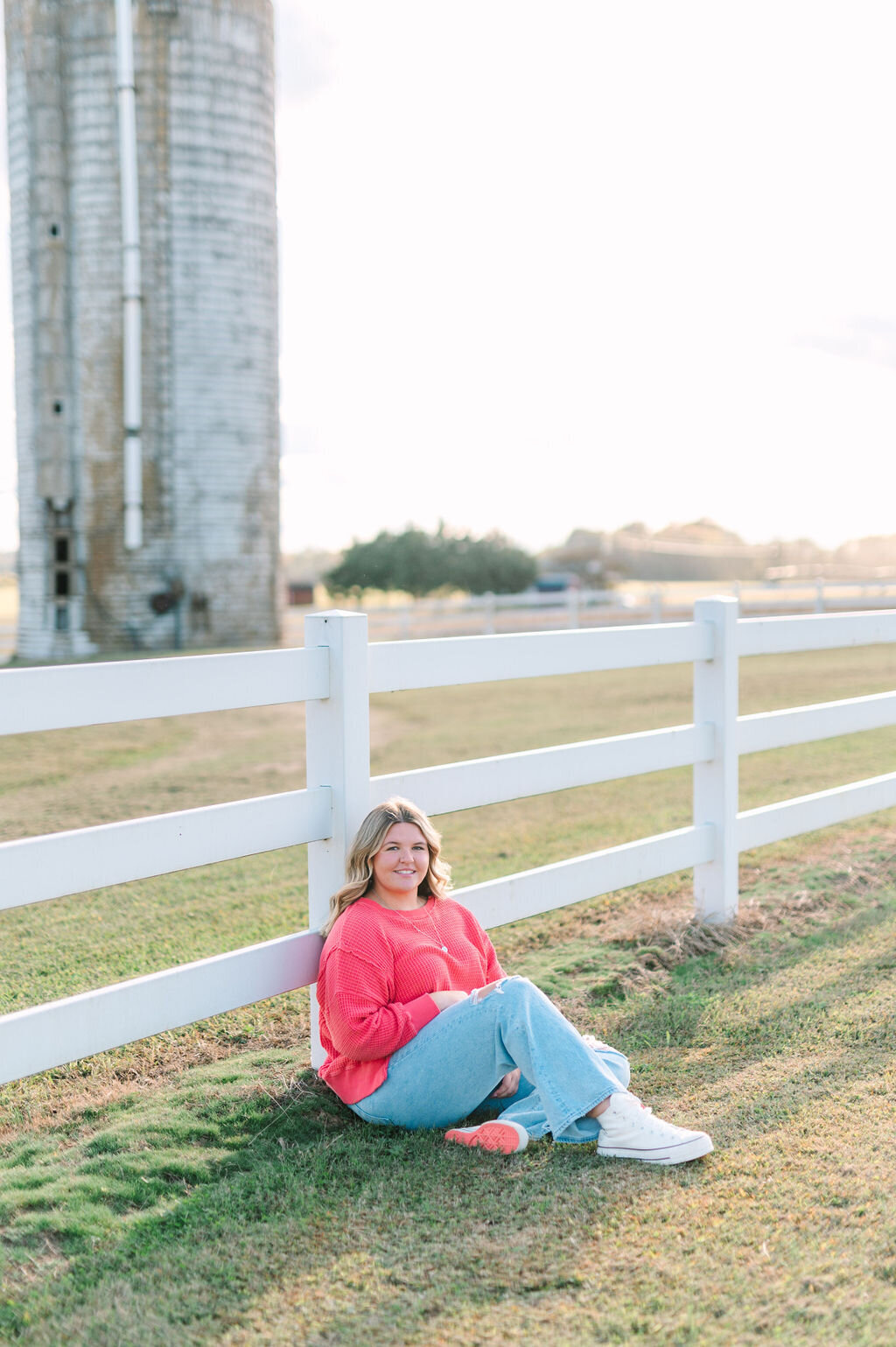 a girl sitting up against a white picket fence