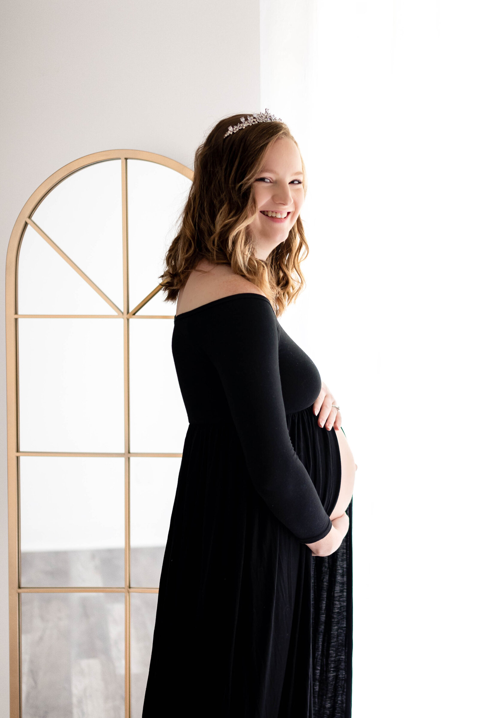 A pregnant woman standing in front of a mirror and holding her stomach for her maternity photos in Huntsville Alabama