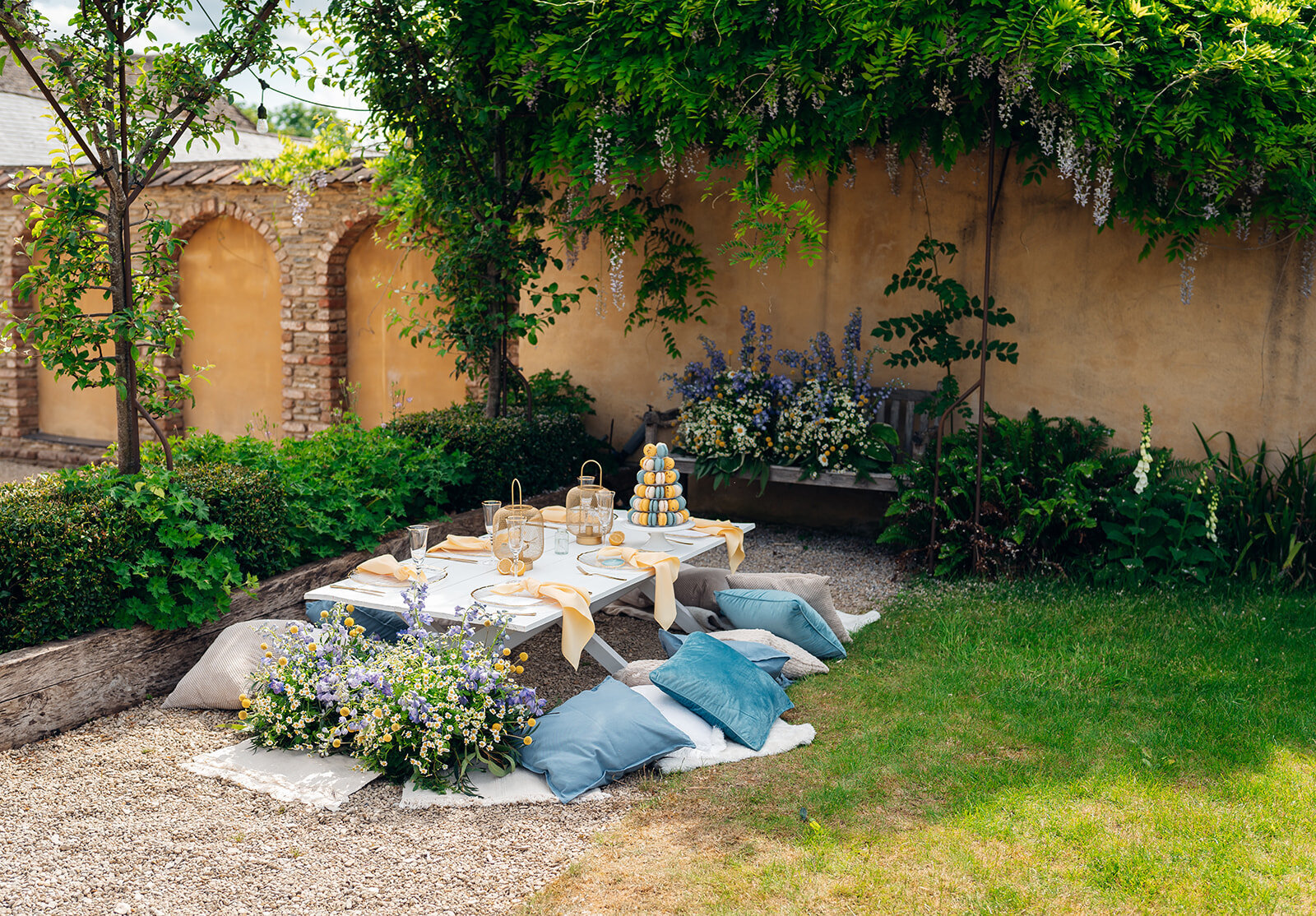 Picnic style wedding breakfast set up, with cushions, grazing boards, macaron tower and floral surrounding. Located at Oxleaze Barn, Cotswolds.