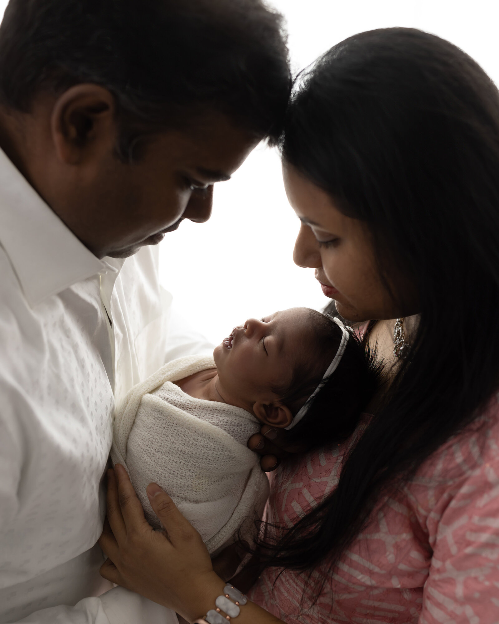 parents holding newborn baby girl wrapped in white for newborn studio portraits