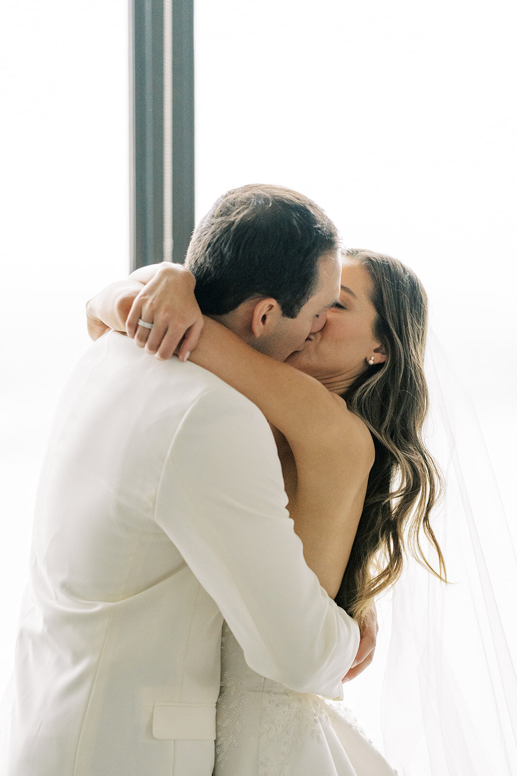 bride and groom kissing in front of window