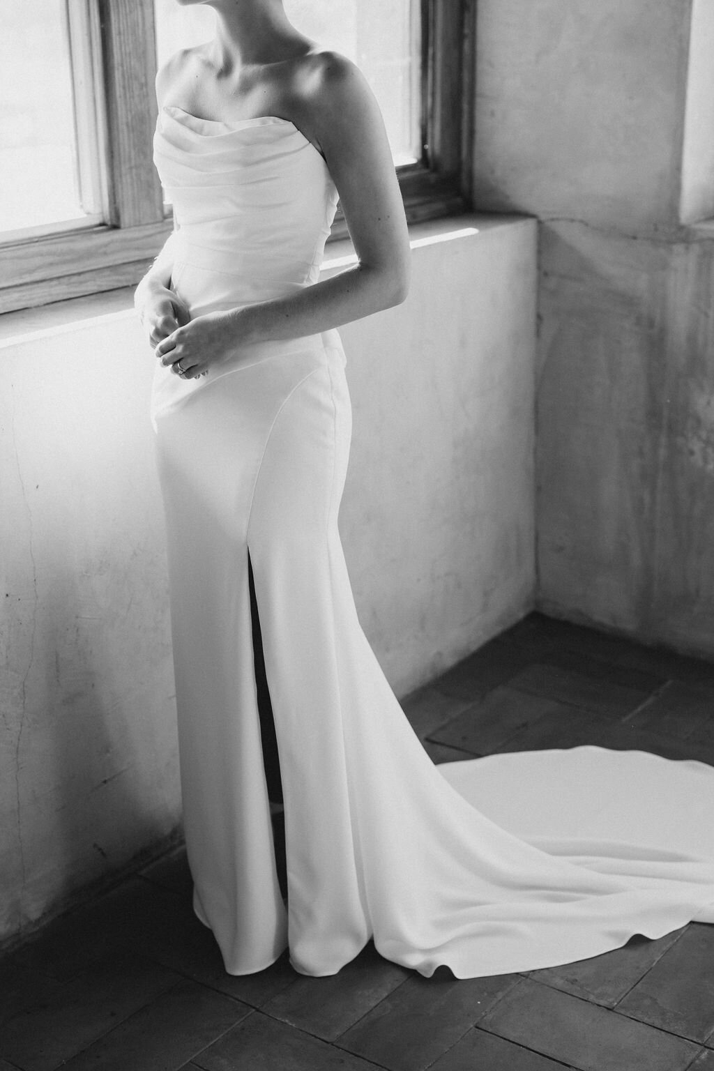 Bride holds hands in white dress by window