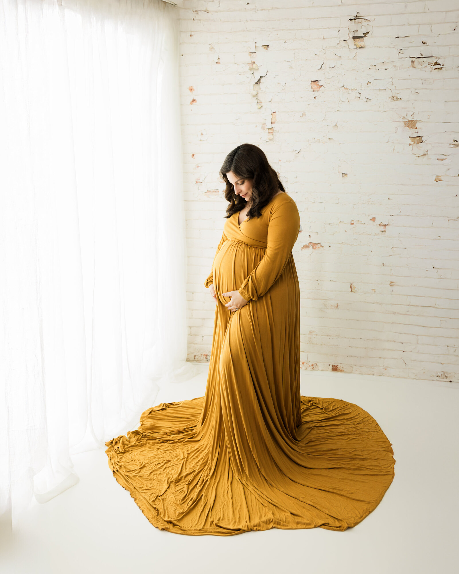 pregnant mother in mustard colored dress holding belly for maternity photoshoot