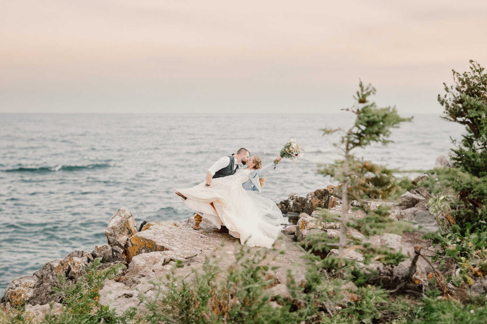 Groom hold his bride and kissing her on the cliff by Lake Superior