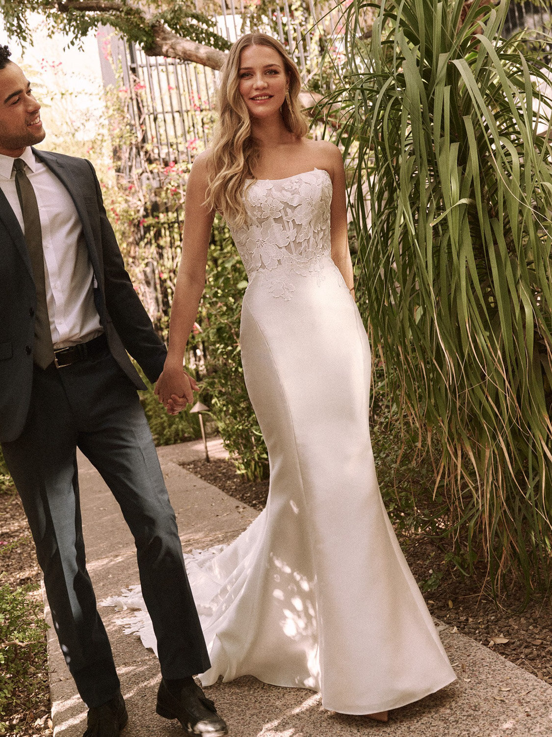 Bride walking hand in hand with groom while wearing a fitted lace wedding gown outdoors