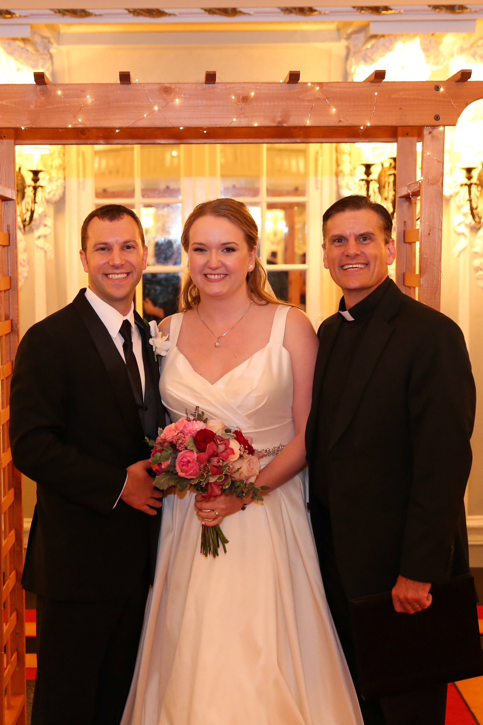 Happy bride and groom pose with their wedding officiant for portrait