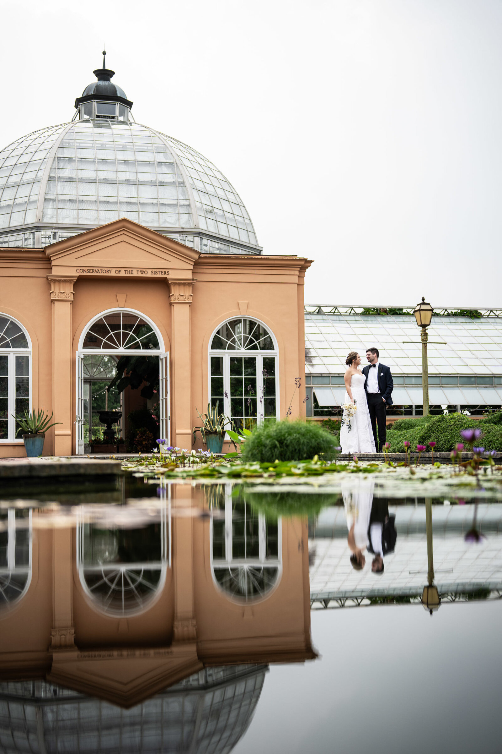 Bride and groom in front of Conservatory in City Park with reflection in lily pond
