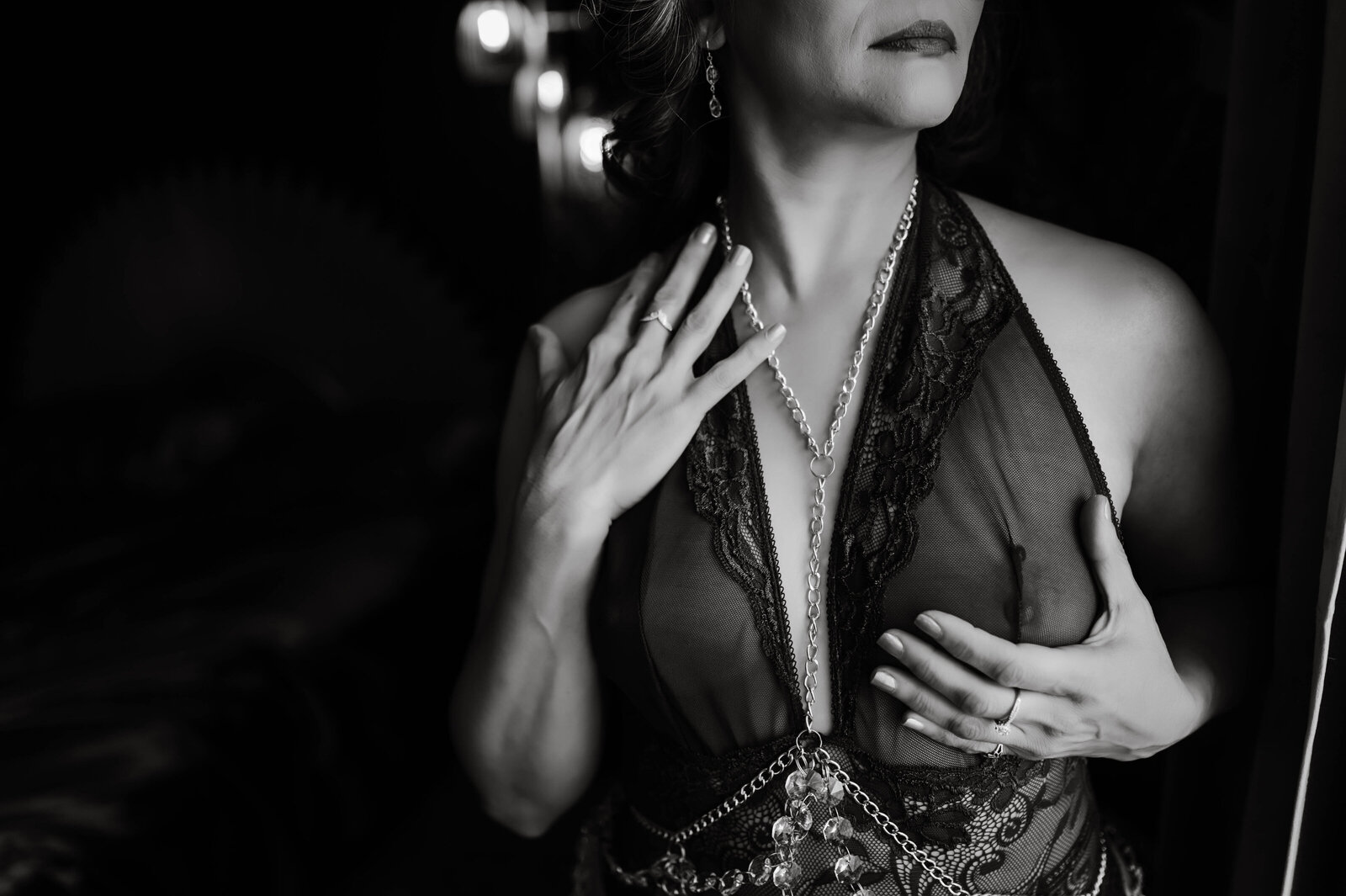 A Boudoir Photography in Memphis image of a woman standing in a window holding a breast in lace sheer lingerie