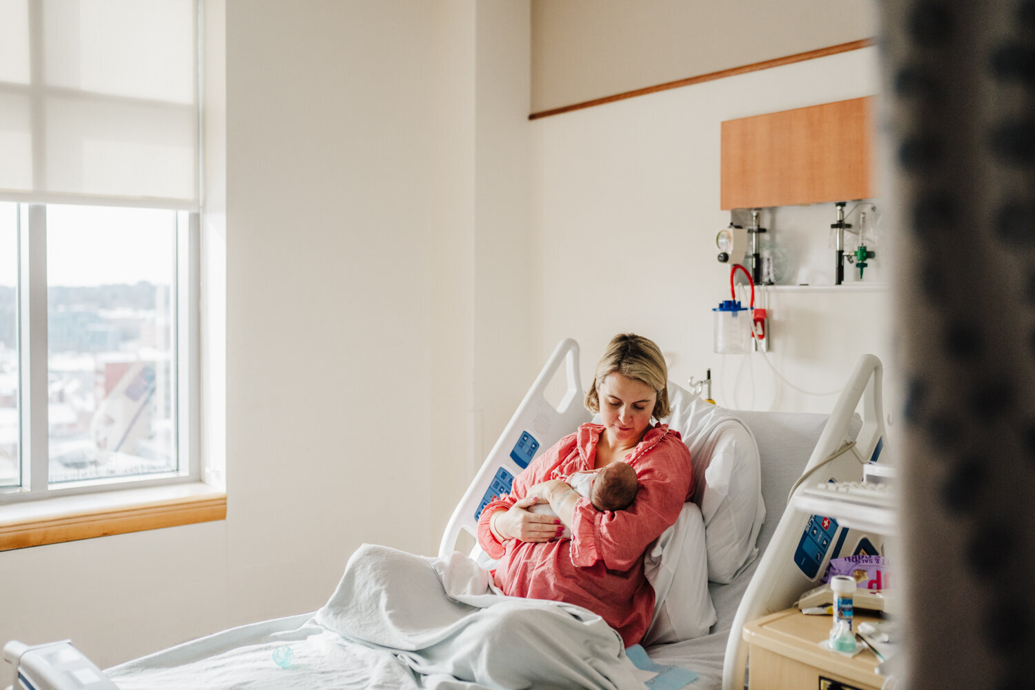 mom stares down at newborn sitting in hospital post partum room in boston