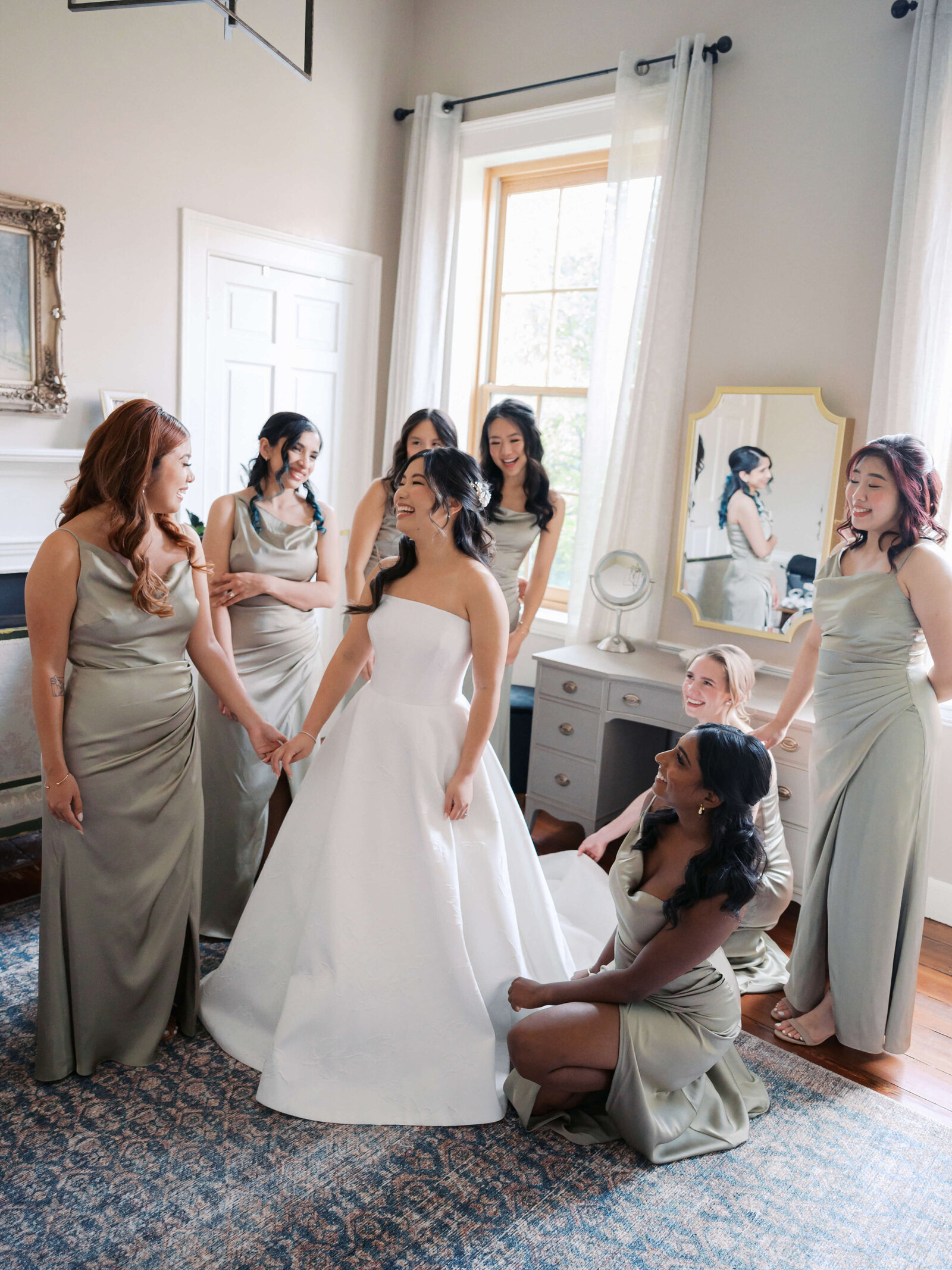 Bridesmaids help their friend the bride get ready inside a chic  white room