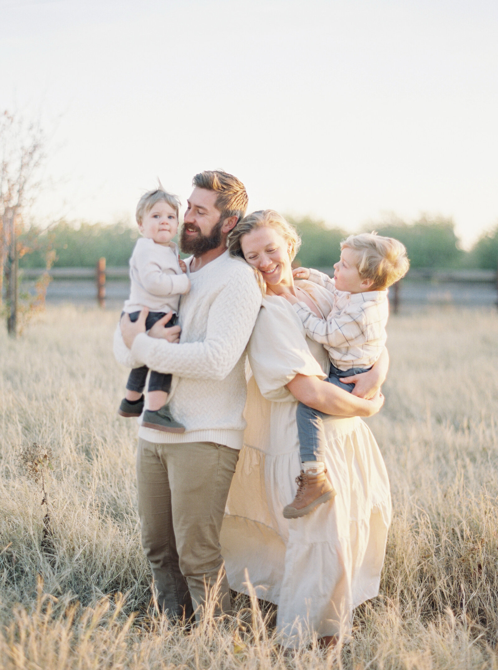 father and mother holding their two children in a field