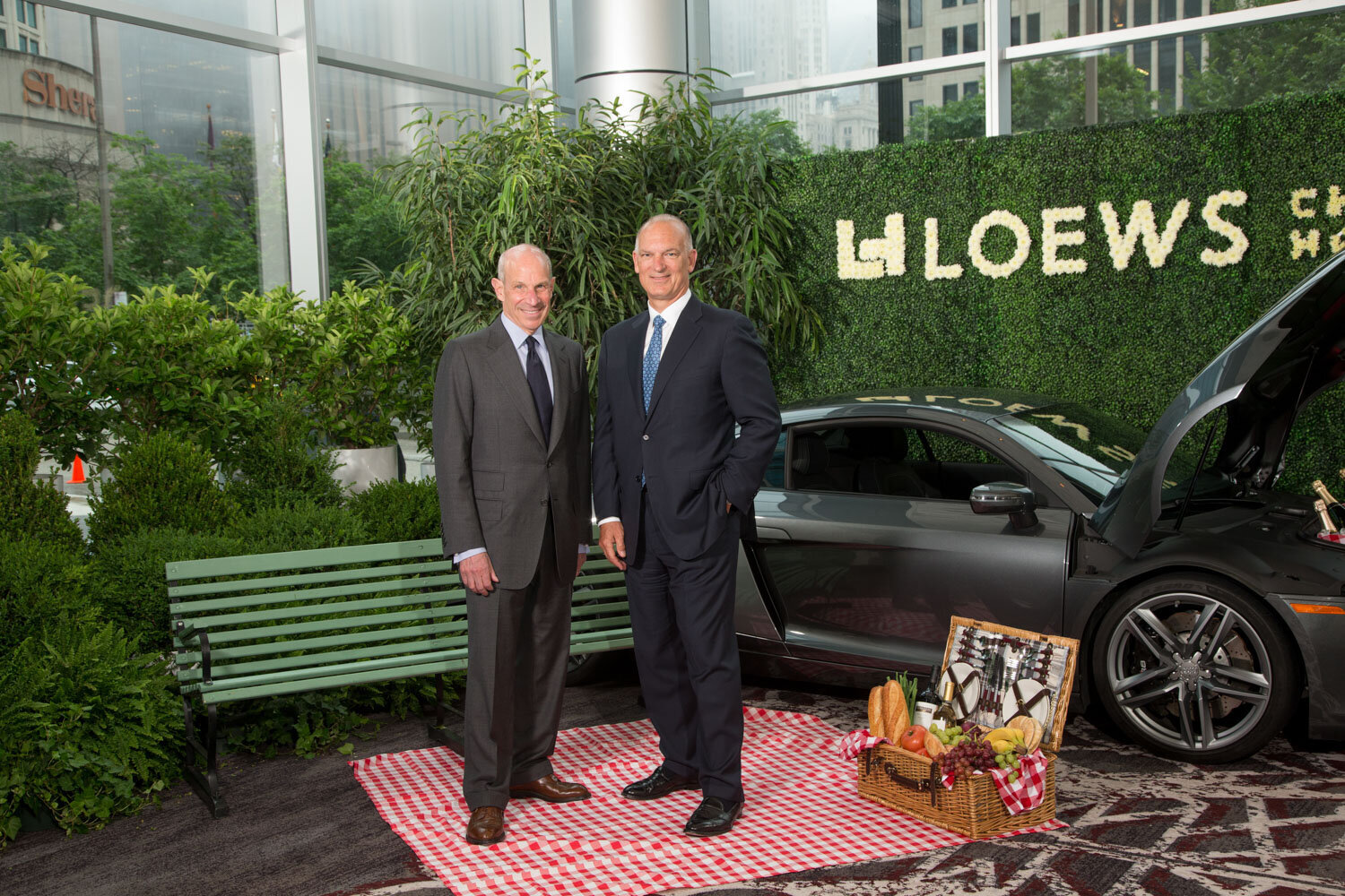 Two men in suits posing on a picnic setup at a Loews event