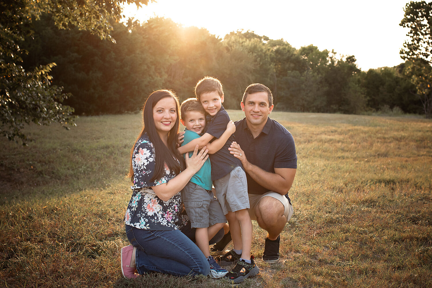 A family hugging in an open field with the sun setting behind them at their family photo shoot with Susan Baraban Photography.