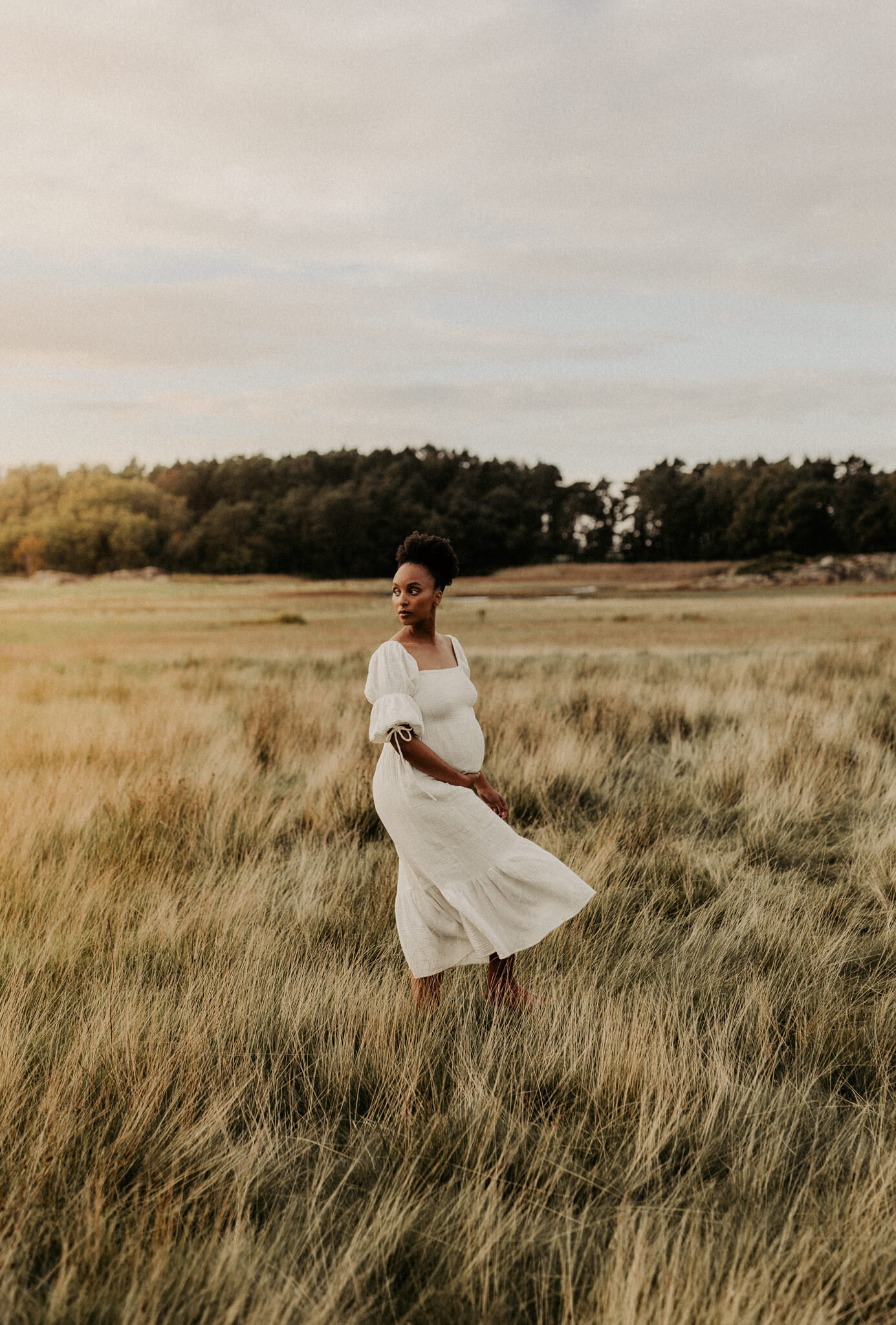 en svart gravid mamma går på ett fält iklädd en vit klänning
