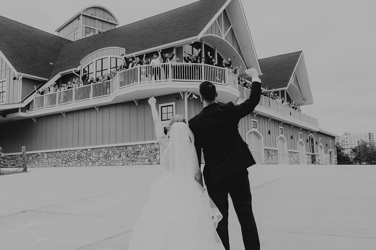 Bride and Groom with arms up to their cheering guests that are at the top deck at Camden County Boathouse