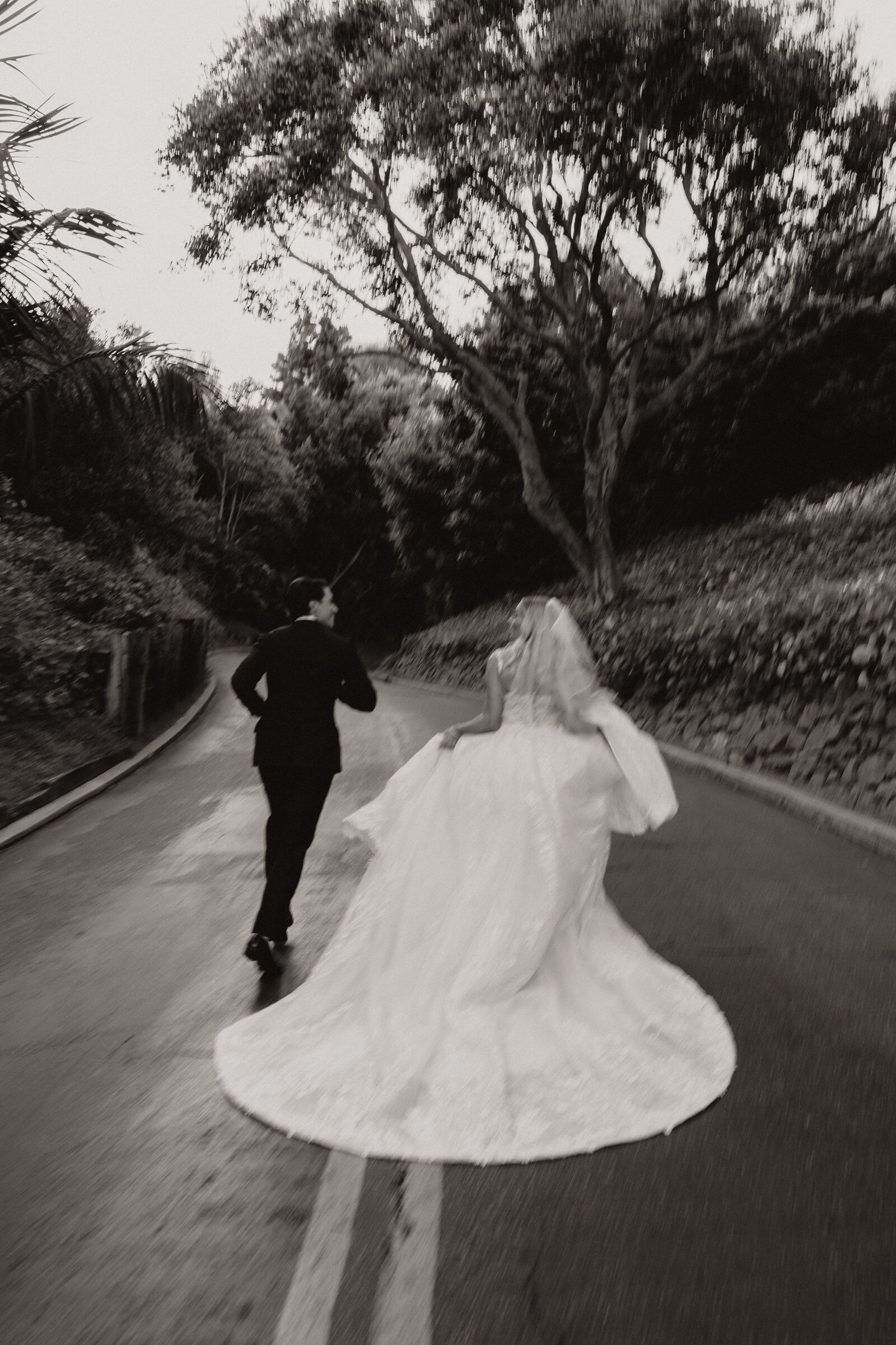Bride and groom running down a tree-lined street during their California wedding.