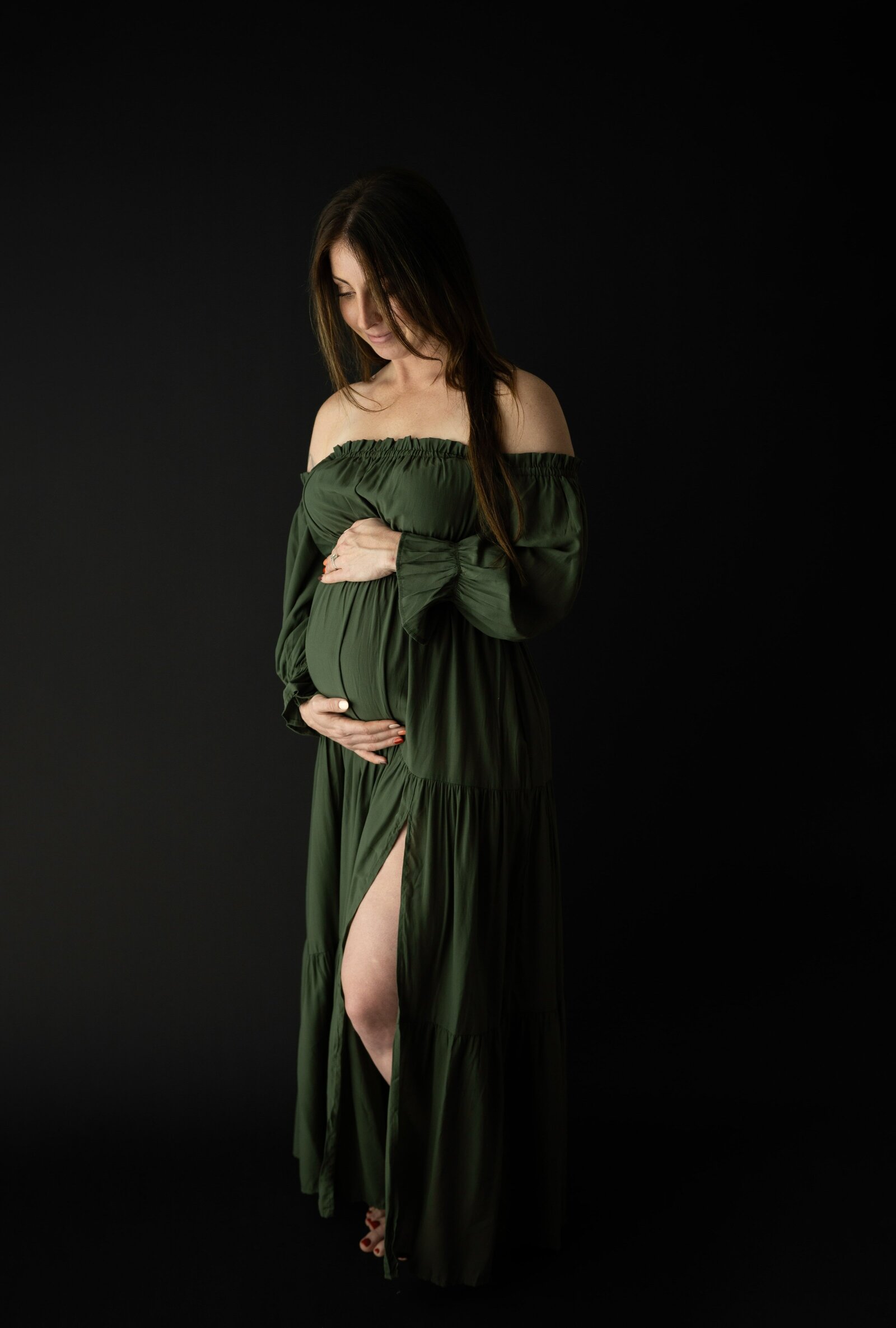 studio maternity session with a woman in a gress dress and black background