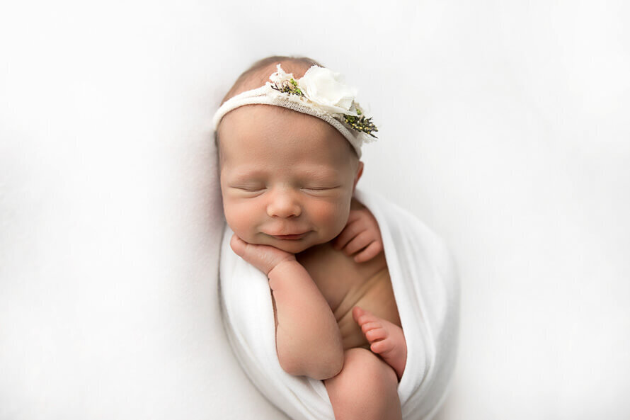 Newborn girl wrapped in white smiiles while sleeping.