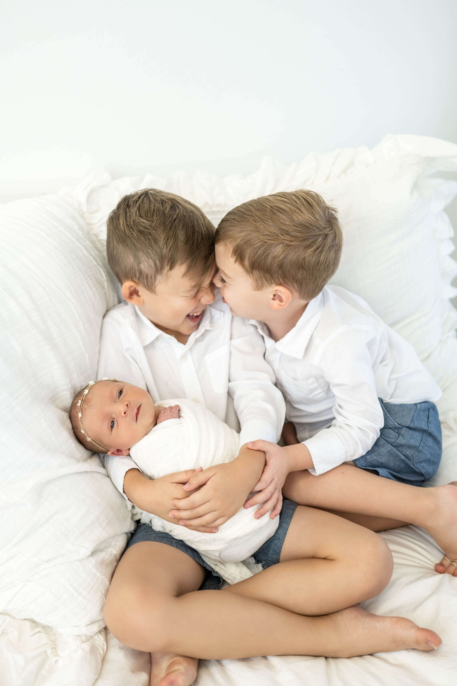 two older brother laughing with glee as they hold their baby sister in their okc metro home
