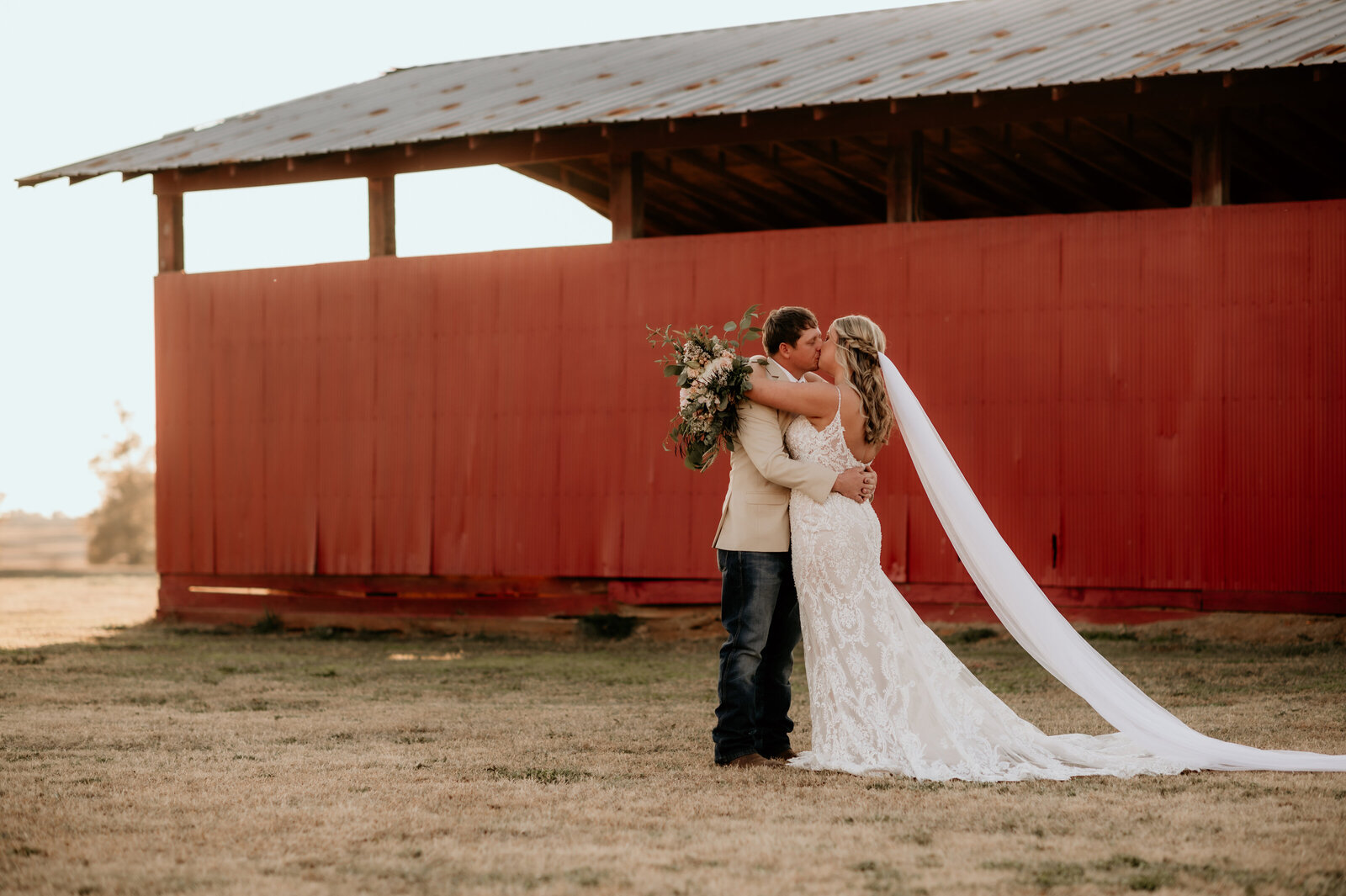 bride adn groom hug each other in front of a red barn captured by Best Little Rock wedding photographer