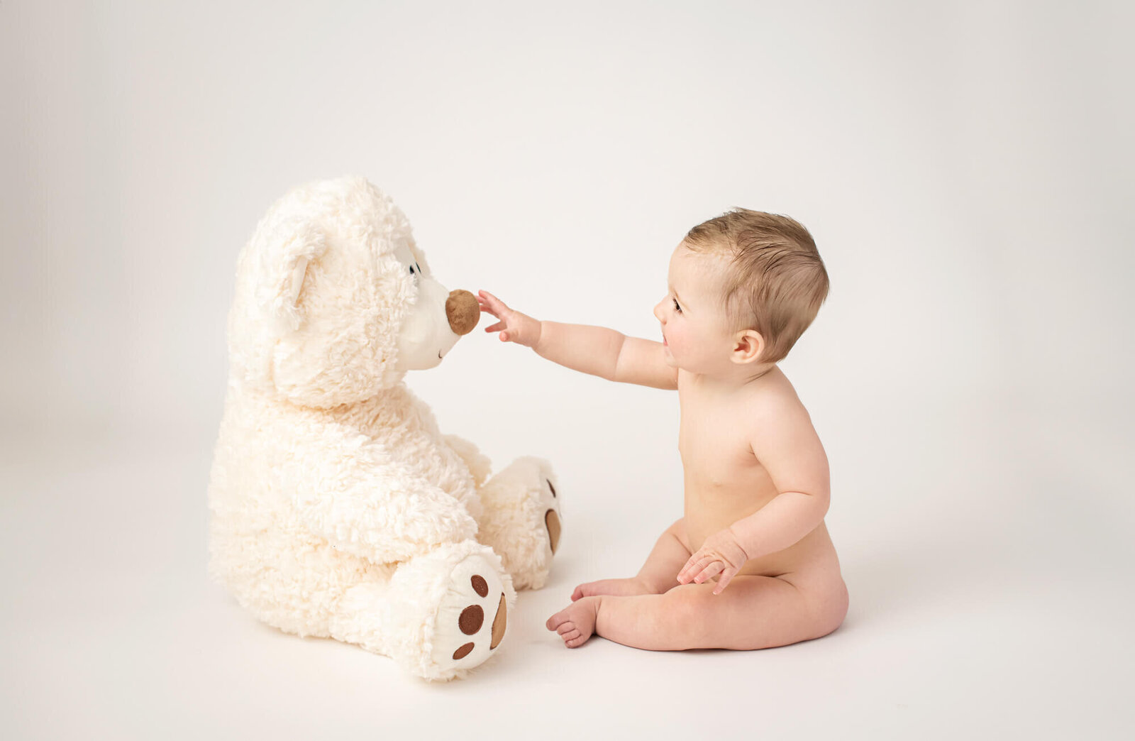 Baby interacting with large white teddy bear