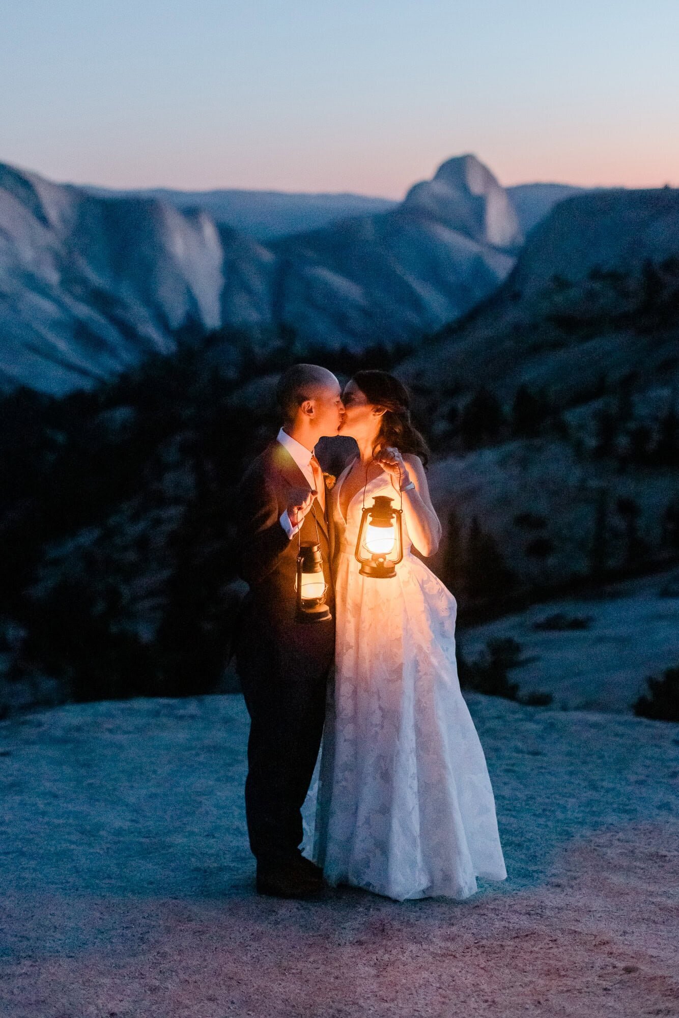 A bride and groom stand in front of half dome past dark, their faces aglow from the light of lanterns, on their Yosemite Elopement Day. 