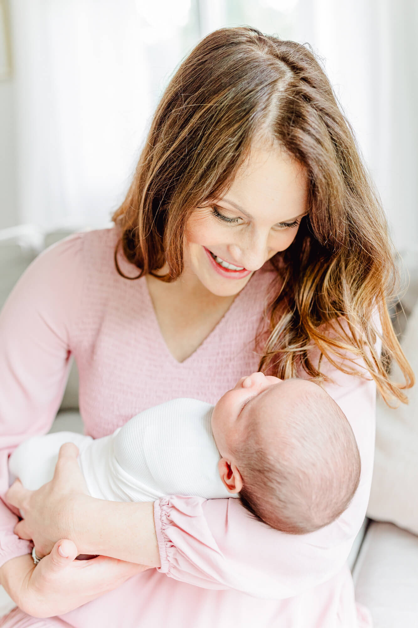 Mom in a pink dress smiling at her newborn on a couch