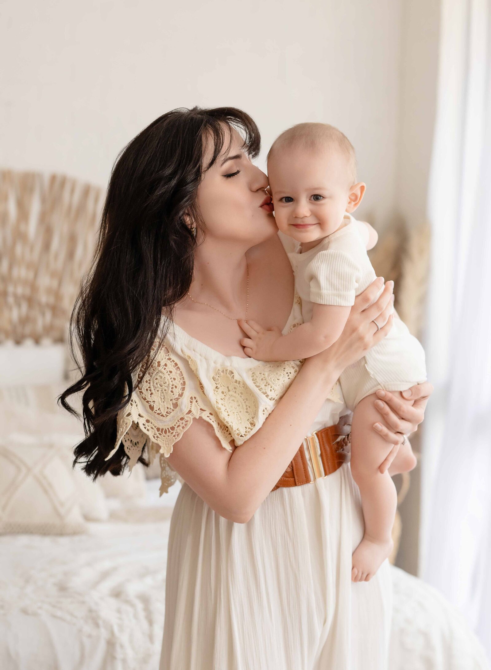 Boho lifestyle bedroom setting with Mom kissing baby on cheek.