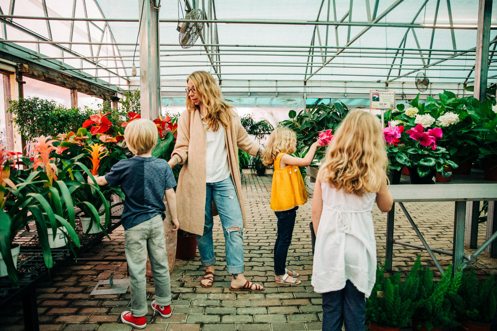 mom in ripped jeans a white tee and beige long cardigan standing in the middle of a plant nursery with young triplets around her