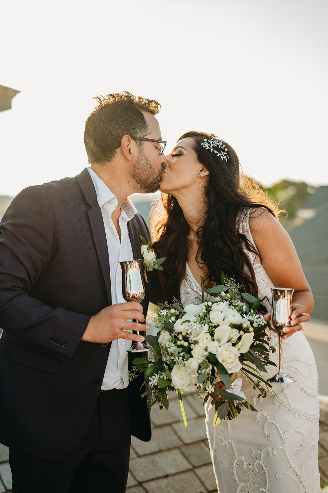 couple kisses after elopement with glasses of champagne