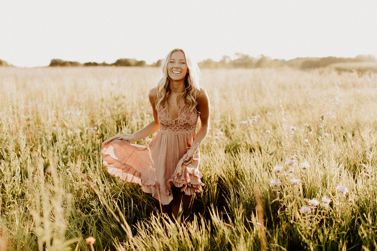 Senior girl standing in a field holding her dress and smiling at the camera