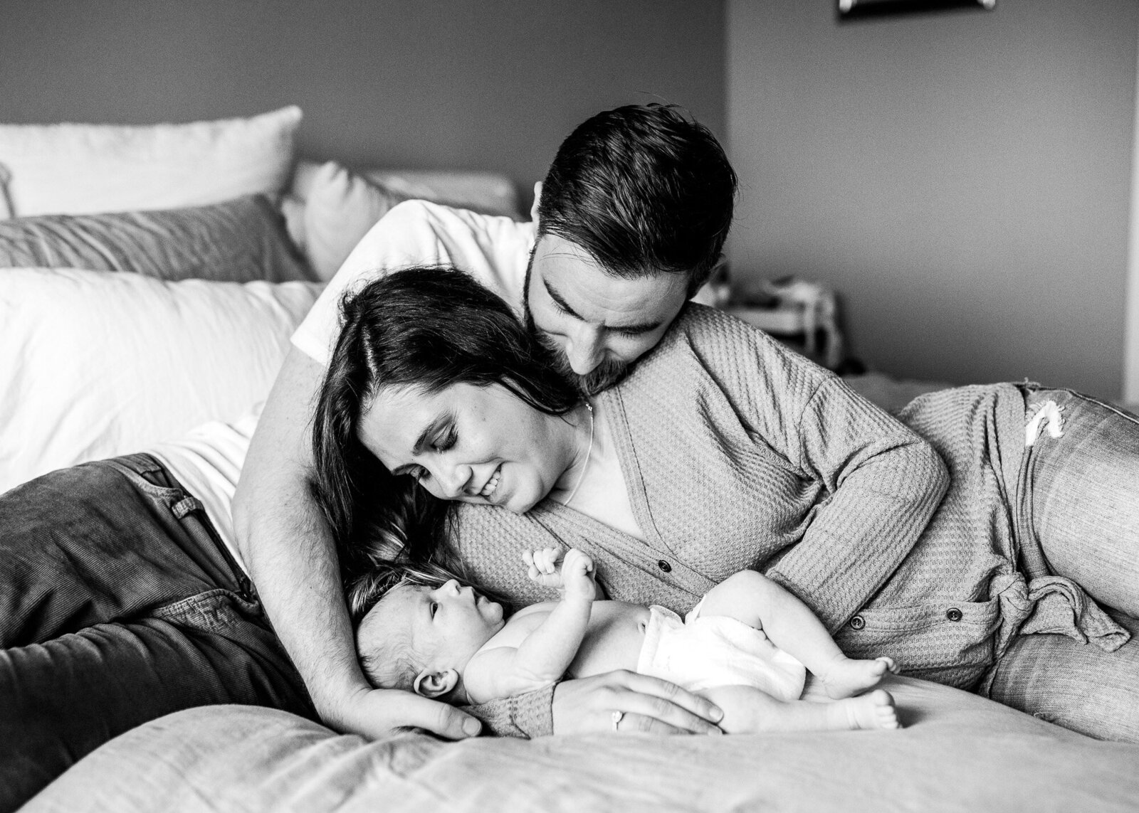 Black and white image of new parents looking at newborn son on bed.