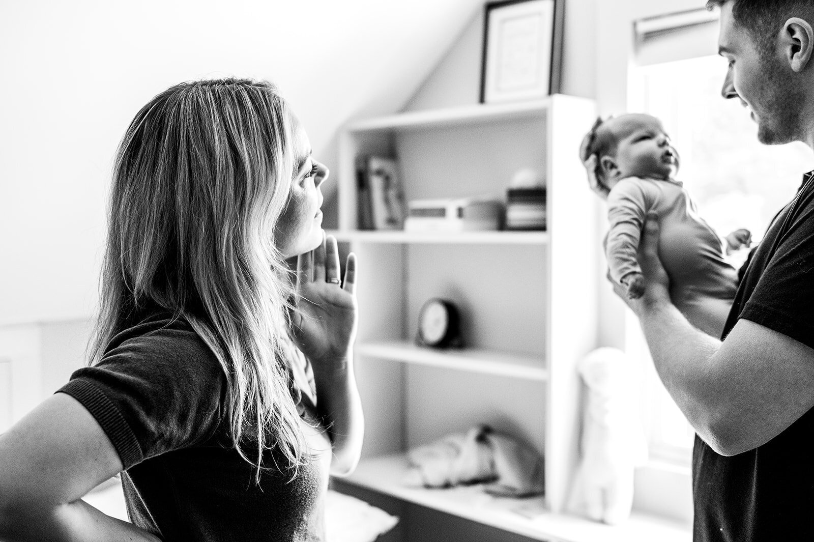 Candid black and white moment of two parents gently dressing their newborn on the bed
