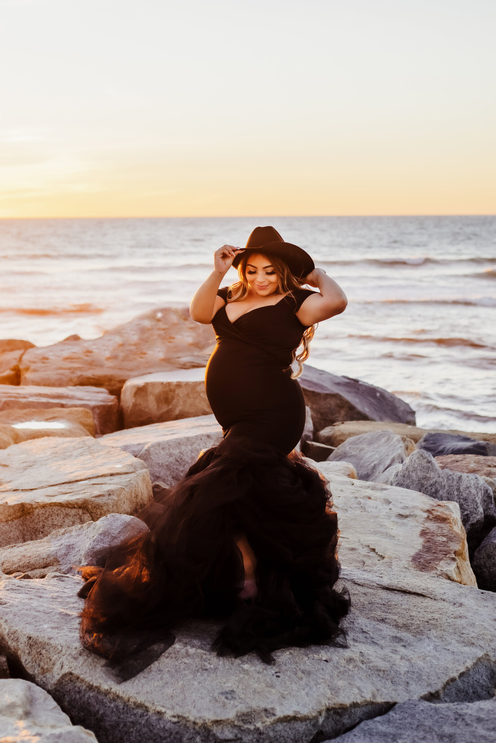 Maternity Photographer, a  pregnant woman wears a black gown and stands near the ocean