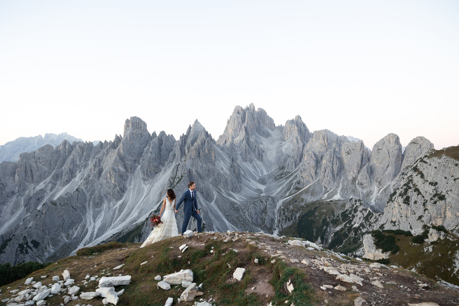 Bride and groom holding hands on a cliff at sunset – adventure elopement photography experience with Kollar Photography.