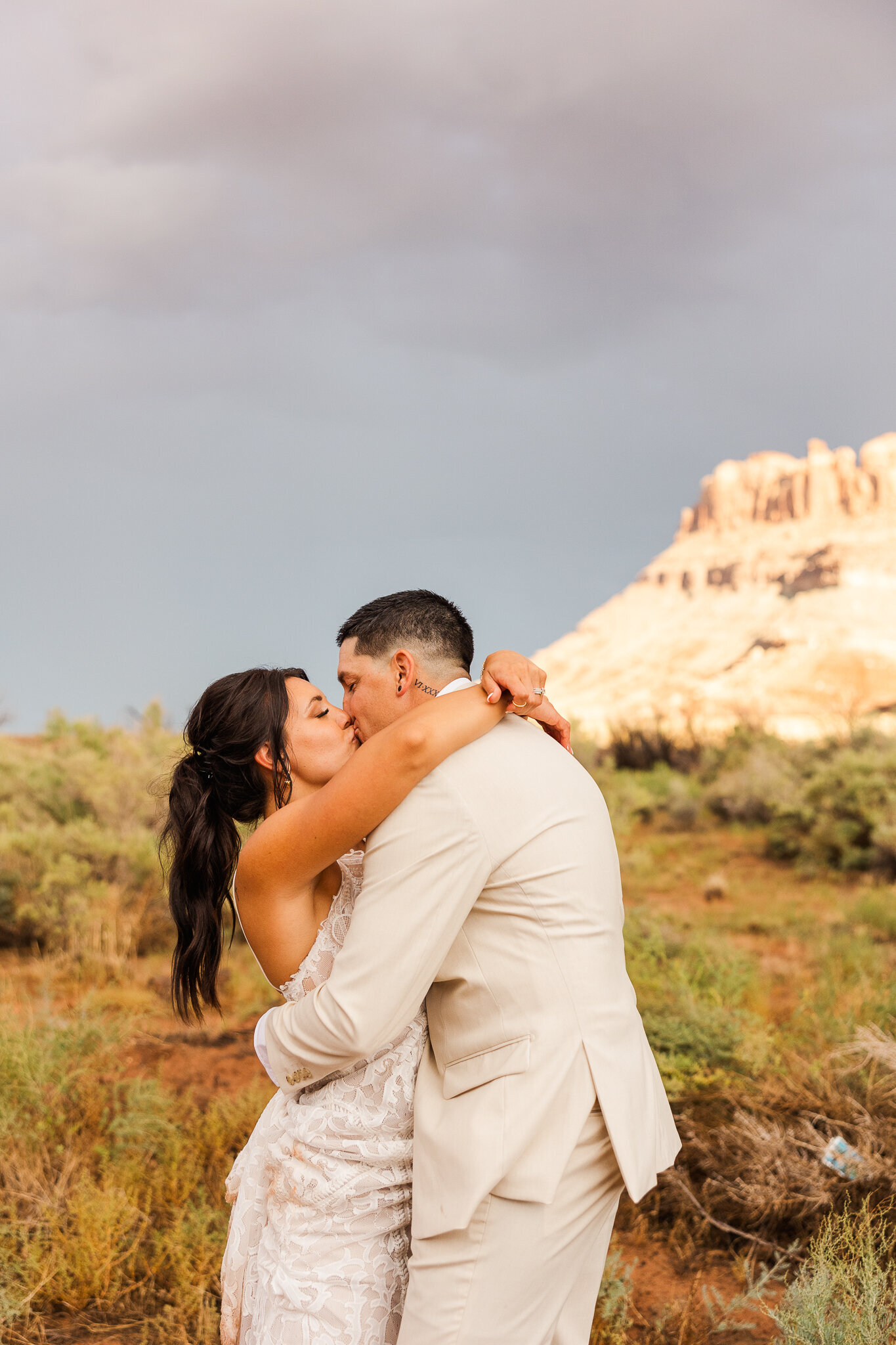 Bride and groom share a kiss during the sunset with the mountains glowing in the back of their red earth venue wedding