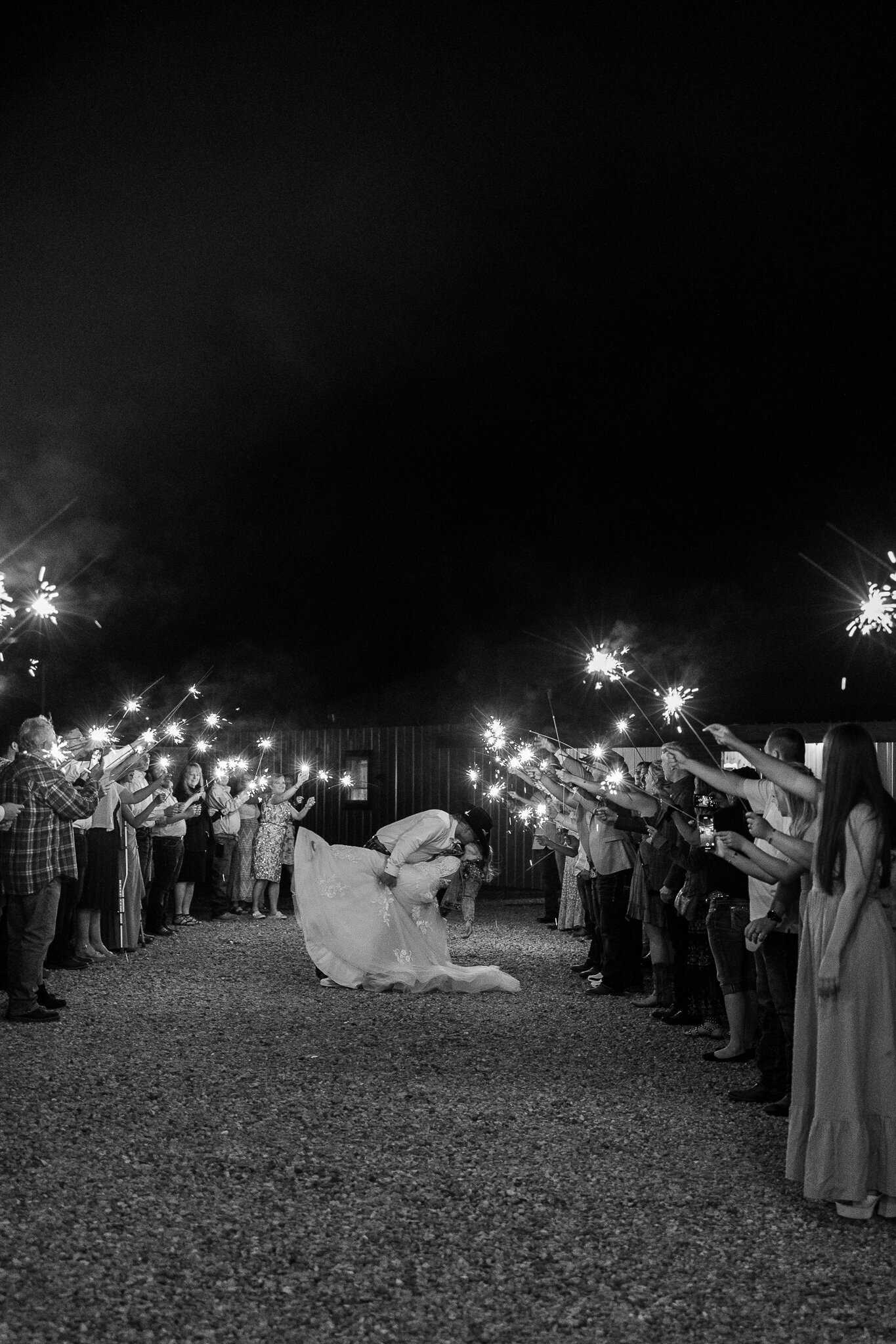Black and white photo of the couple’s sparkler wedding exit surrounded by cheering guests at Absolute Prestige in Loma, Colorado.