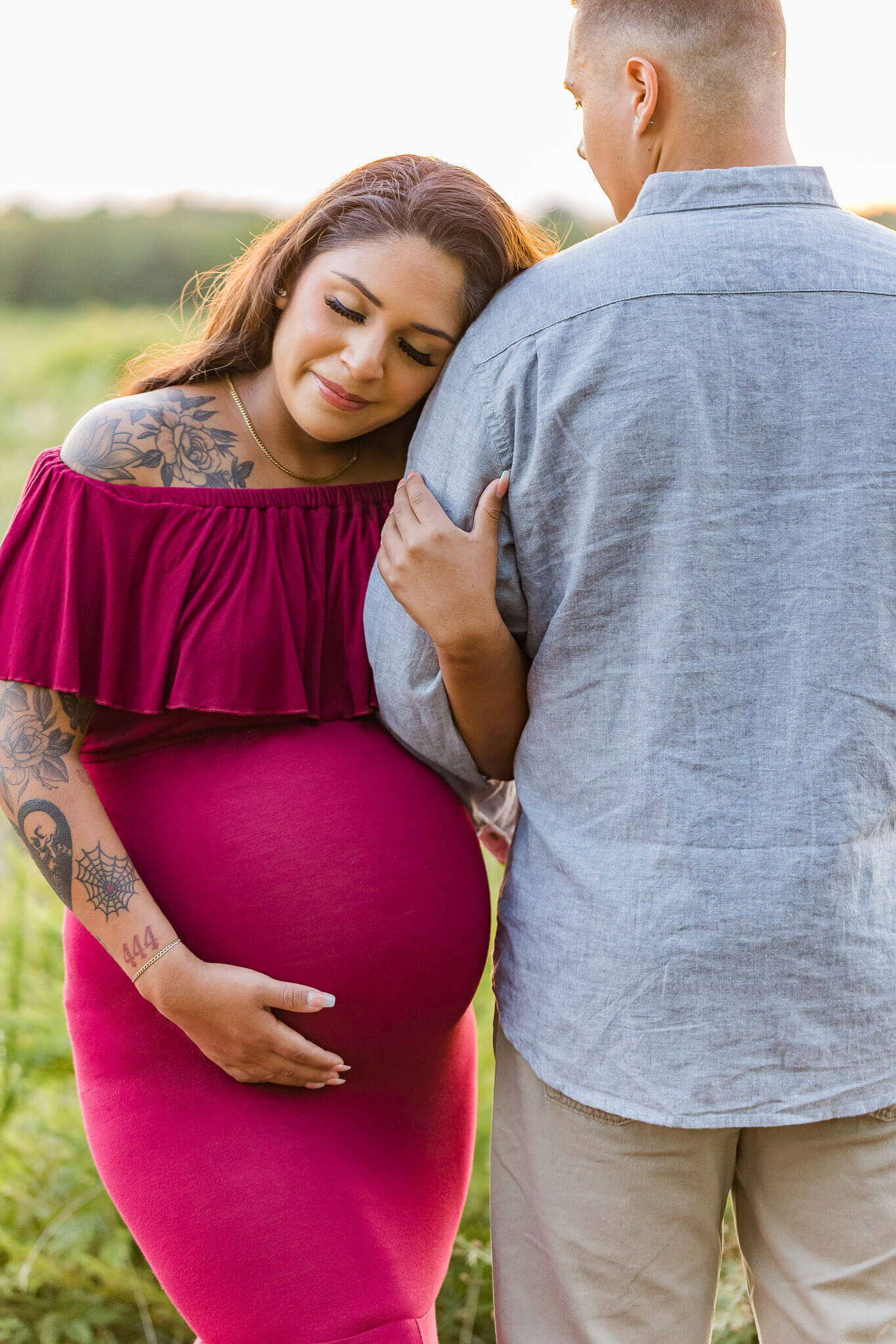 A pregnant woman in a red dress holding her belly and snuggled onto dad's shoulder.