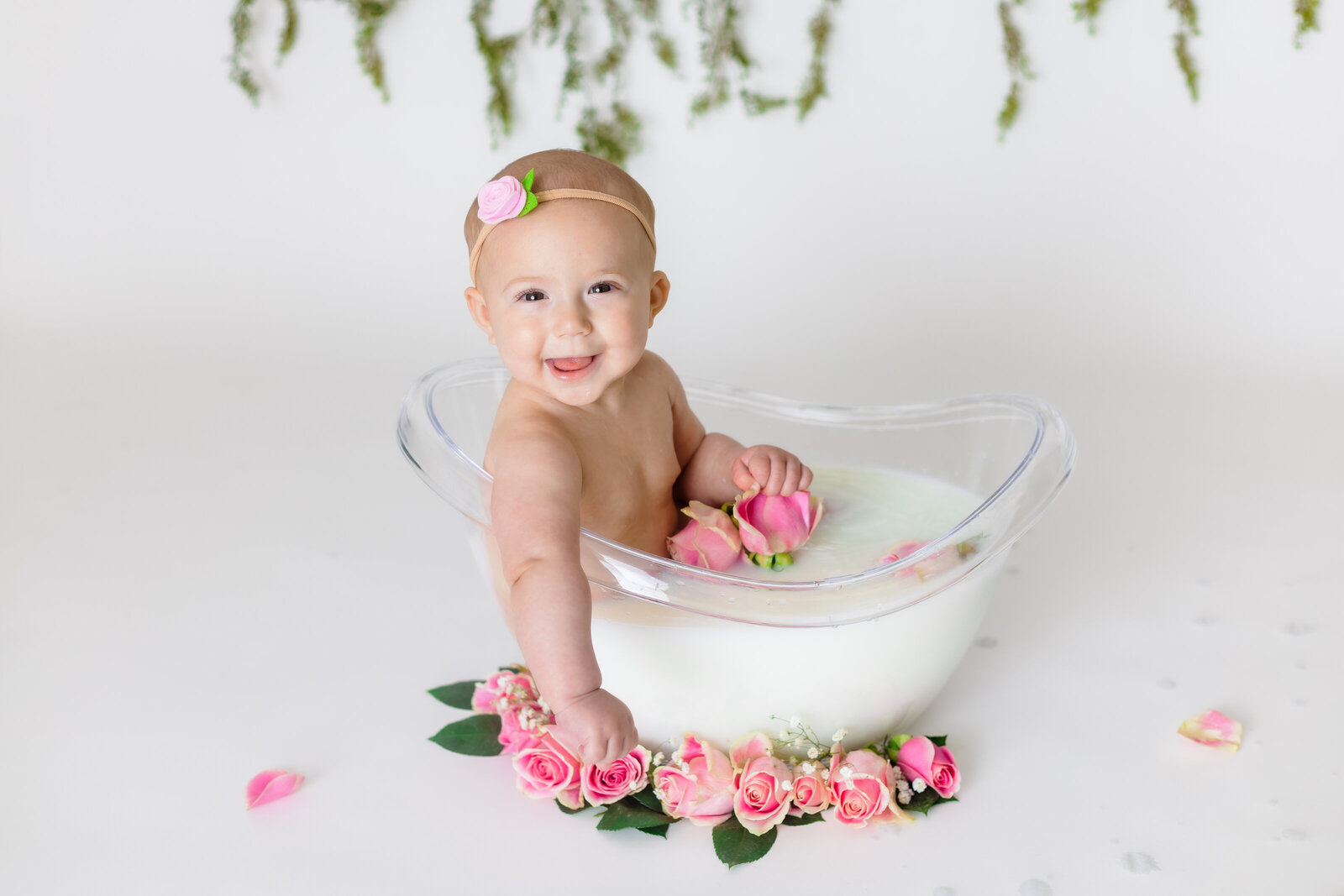 Milestone Photographer, a baby sits in a glass tub with flowers and smiles