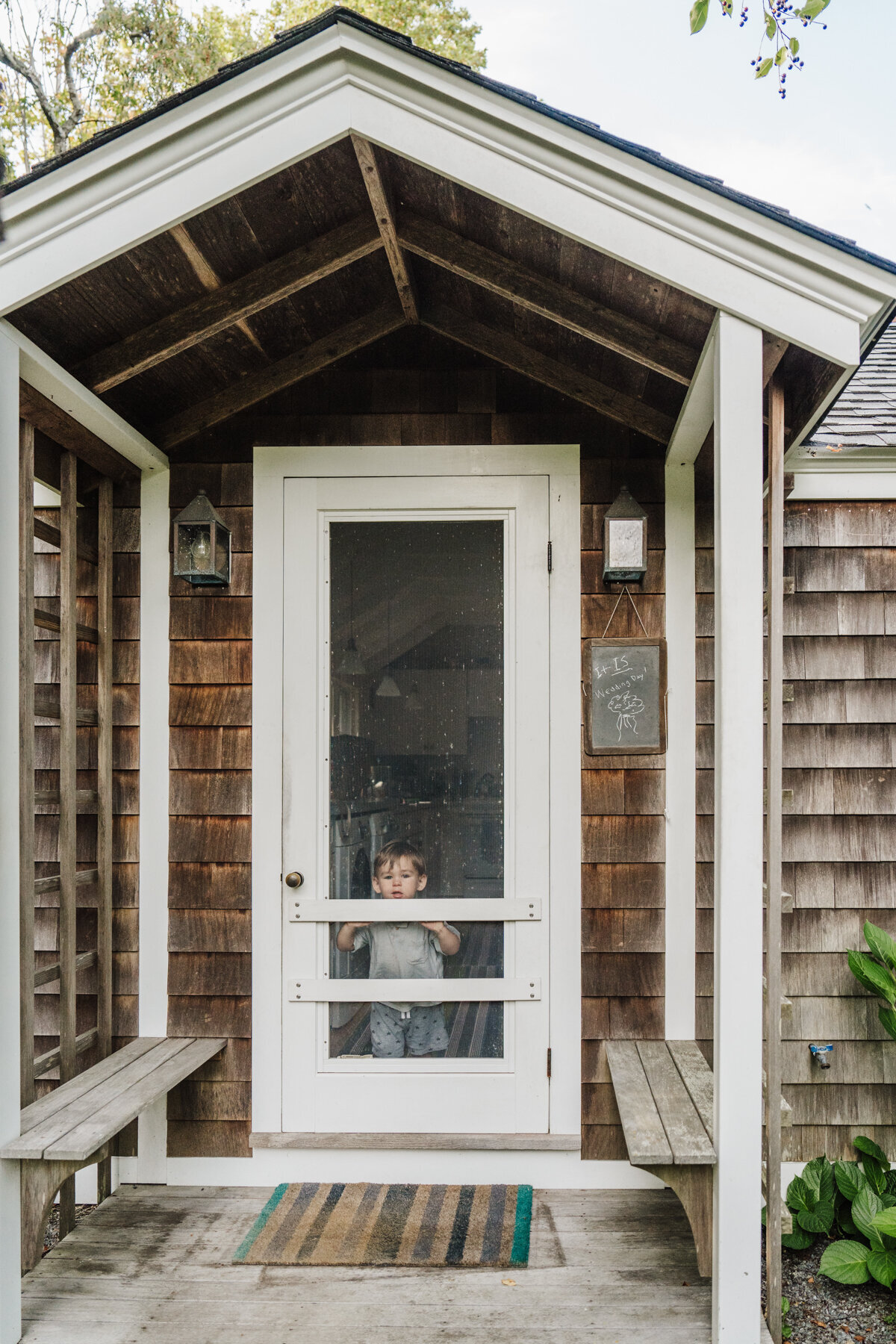 little boy looks through screen door of cottage on wedding day