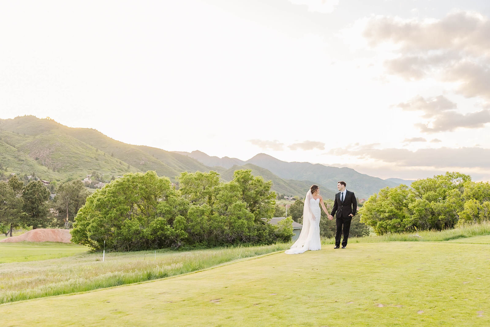 Bride and groom walking hand in hand across the lush greens of Arrowhead Golf Course in Littleton, Colorado, during their romantic wedding celebration.
