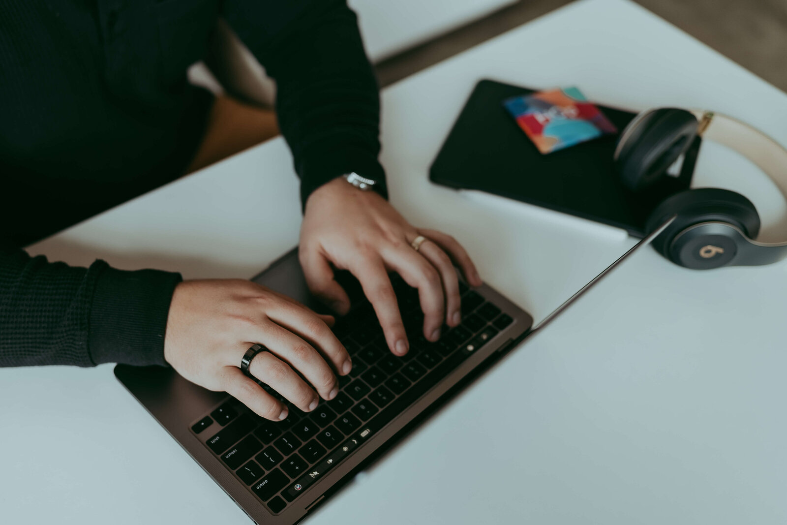 A close-up image of a man's hands working on his laptop as the product that he sells is sitting next to him.
