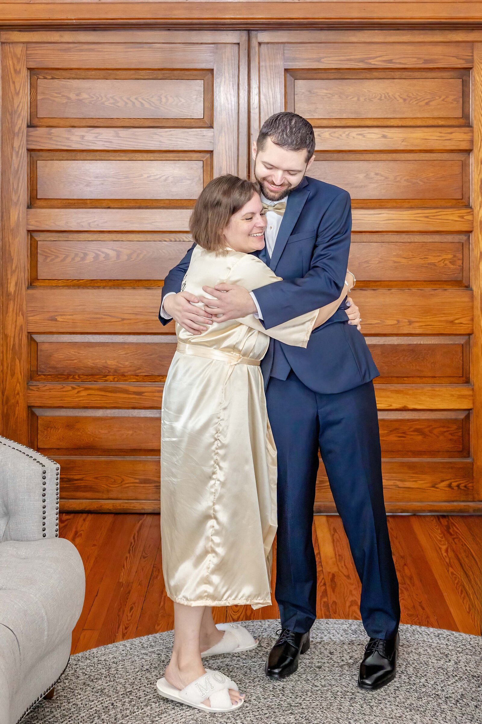 A heartwarming moment as the groom embraces his mother in a bridal suite with rustic wooden doors, captured during an elegant Boone, NC wedding.
