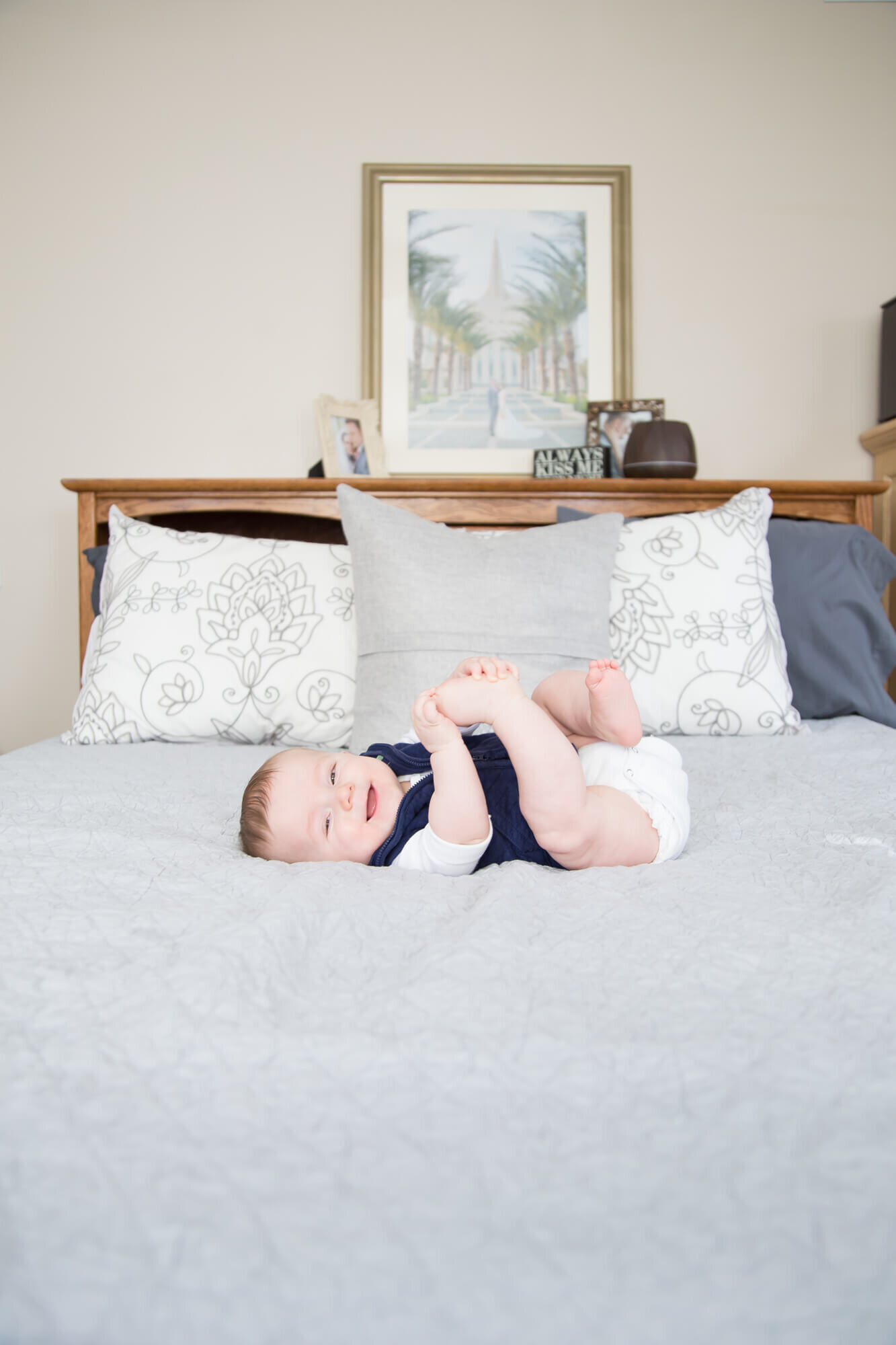 Infant boy happily playing iwth toes on a bed during his session with las vegas milestone photgrapher