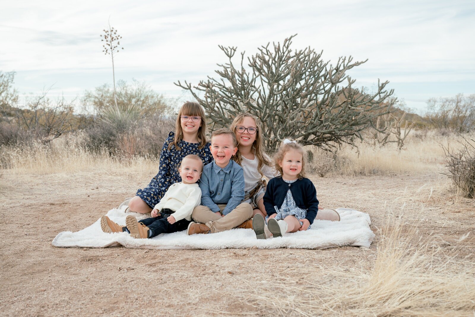 little kids sitting on a blanket smiling at camera 