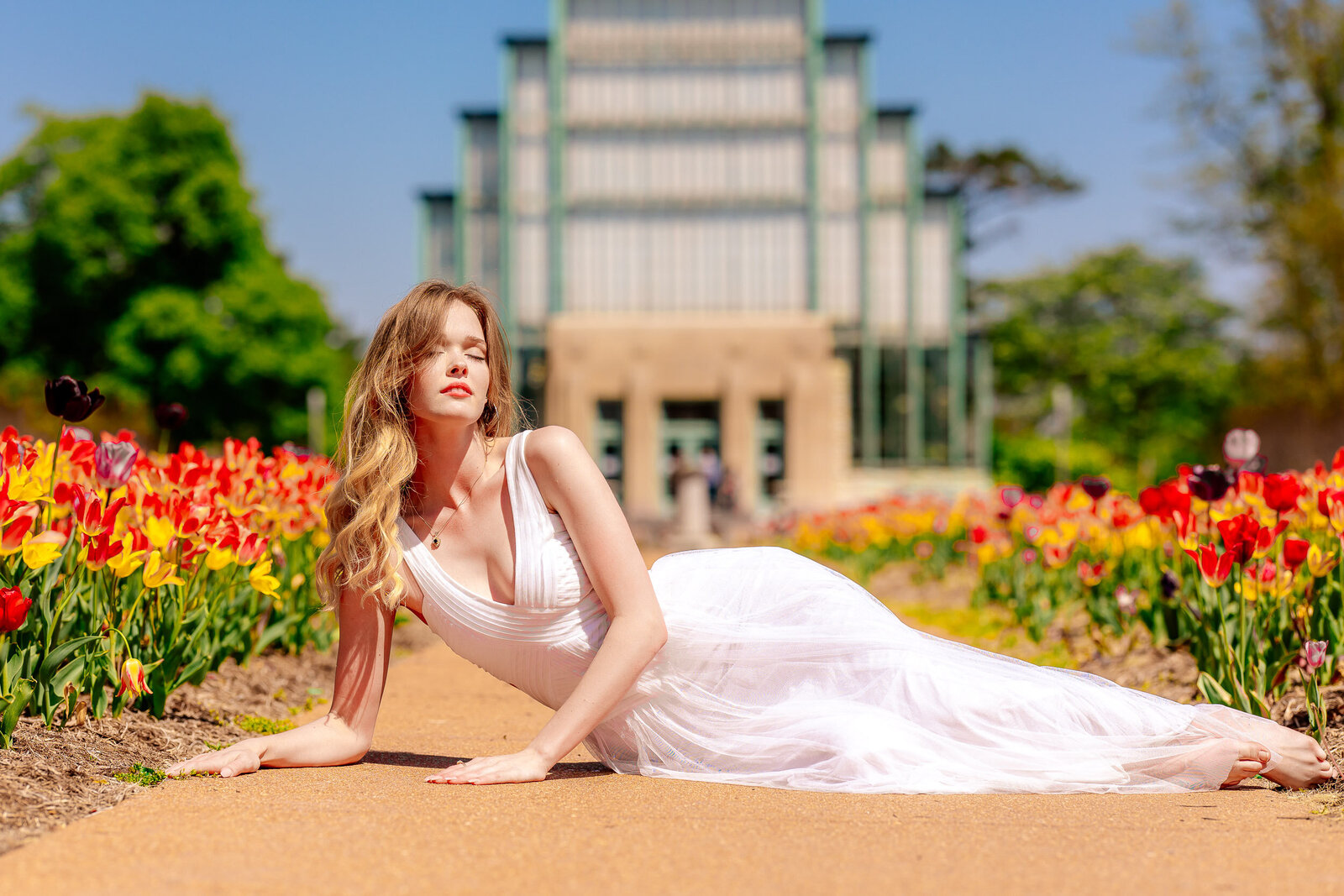 senior laying down in front of the jewel box in forest park in between the tulips in white dress