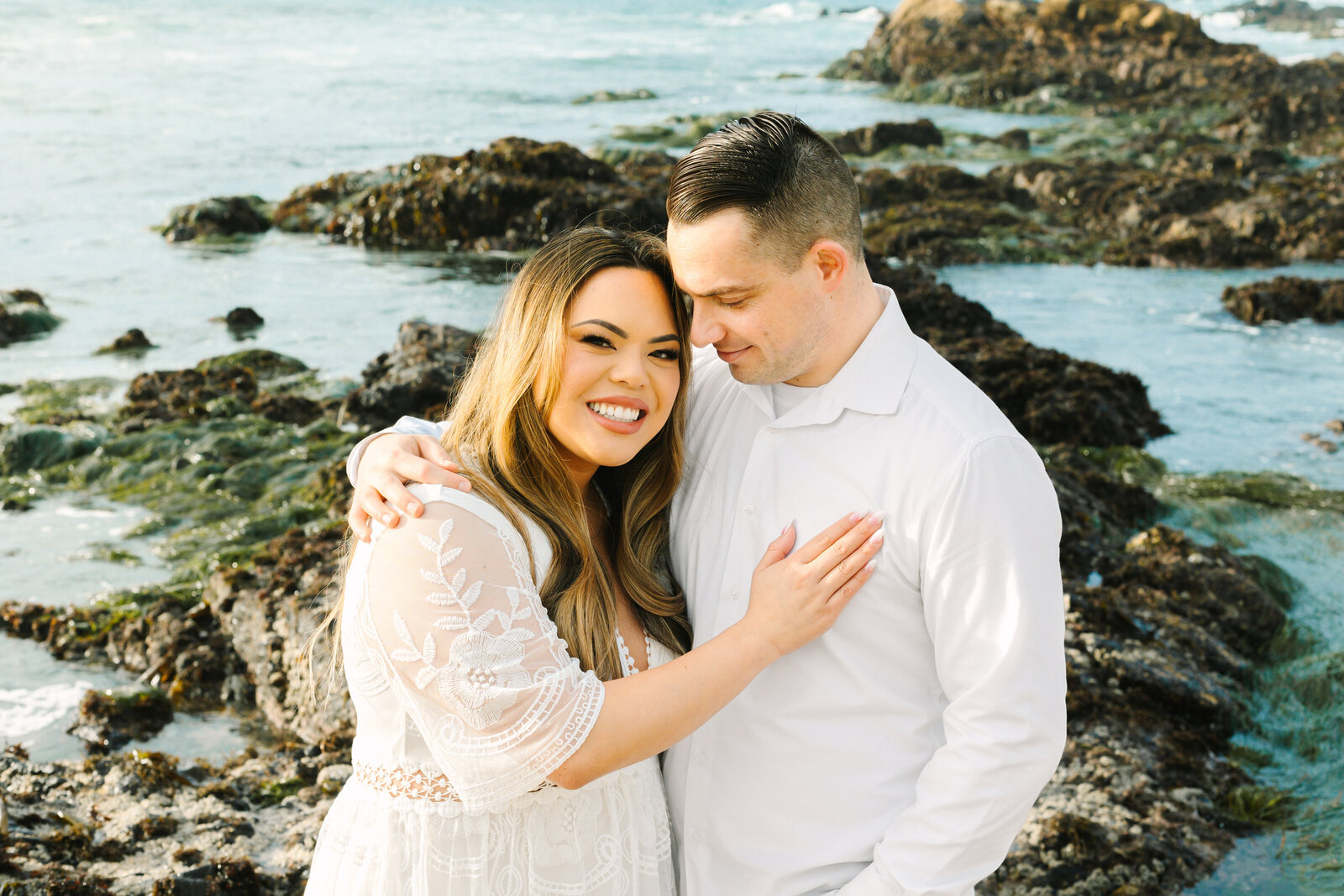 An engaged man and woman take photos on the beach in Pacific Grove, Monterey, California near Big Sur.
